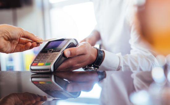 Hand of customer paying with contactless credit card with NFC technology. Bartender with a credit card reader machine at bar counter with female holding credit card. Focus on hands.