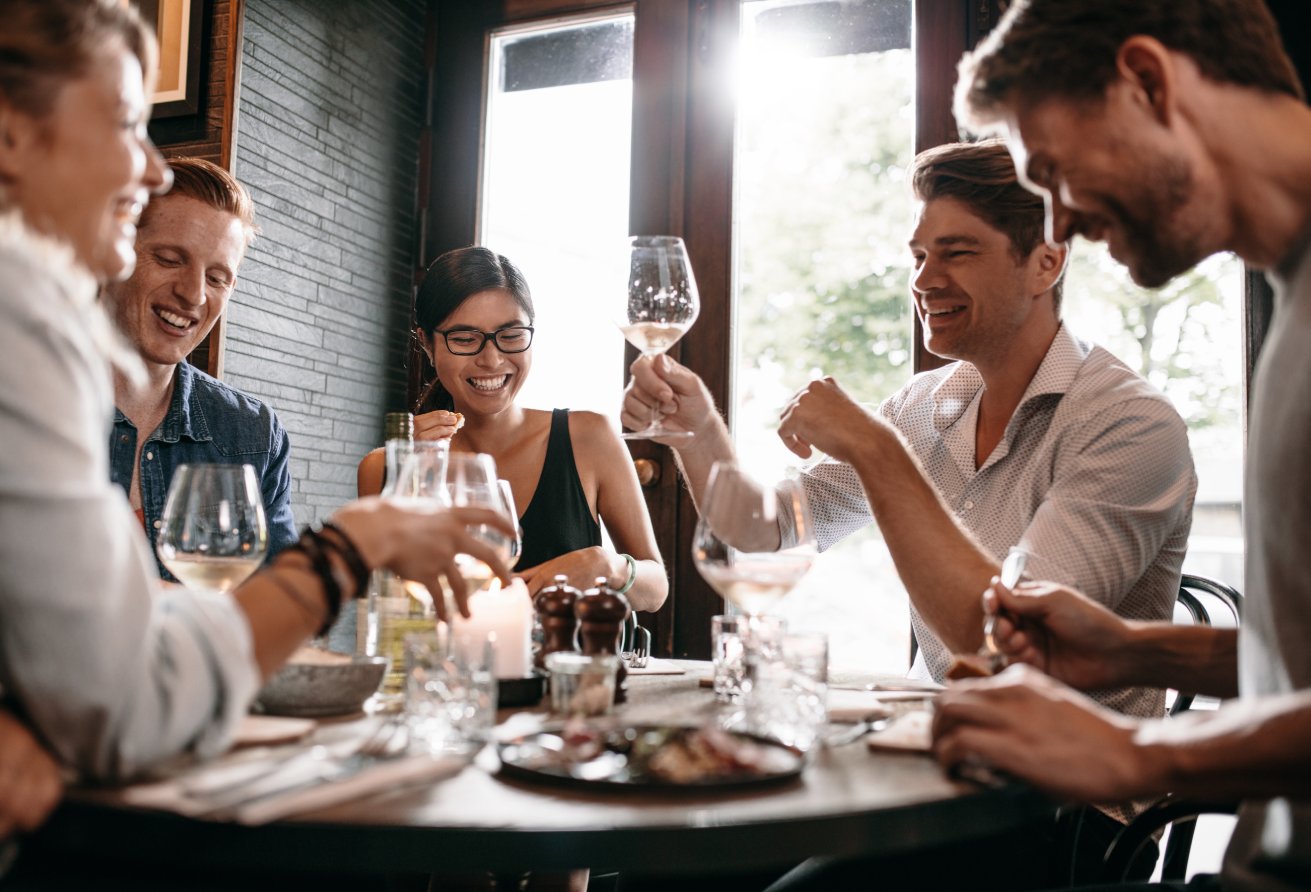 Young man raising his glass of wine with friends at restaurant. Young people enjoying dinner at a cafe.