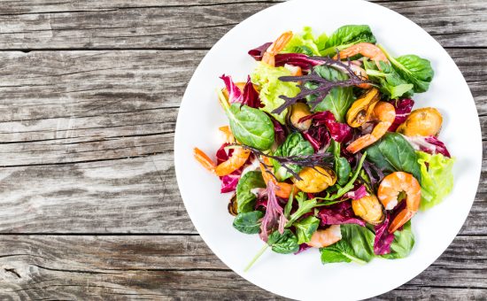 delicious fresh salad of prawns,mussels and mixed lettuce leaves - baby spinach, arugula, radicchio rosso in the white dish on the old wooden table, top view