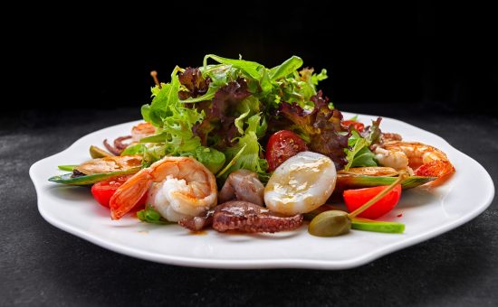 Mix salad with seafood shrimp, scallop, octopus, squid, tomatoes and lettuce on a dark background