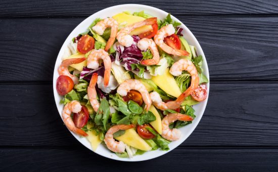 Mix of salad with shrimps , avocado and cherry tomatoes . Healthy food background