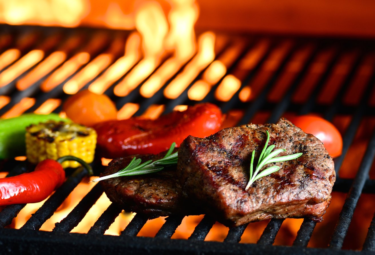 Delicious meat and vegetables grilling on open grill, bbq. Steak and vegetables char-grilled over flame, garnished with slices of peppers, corn, carrots, and fresh twigs rosemary. Cooking in Josper.