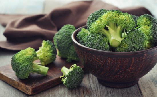 Bunch of fresh green broccoli on brown plate over wooden background