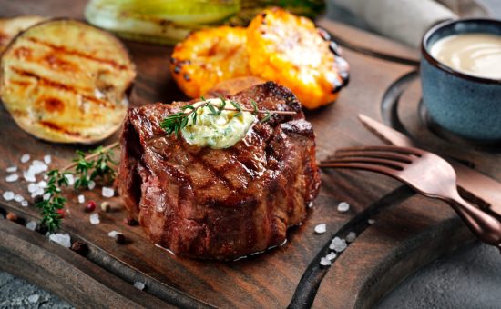 Grilled beef tenderloin steak on a wooden board with butter and thyme. Filet Mignon recipe with vegetables